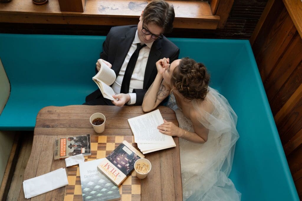 Couple reading a book together dressed up as a Bride and groom inside a cafe