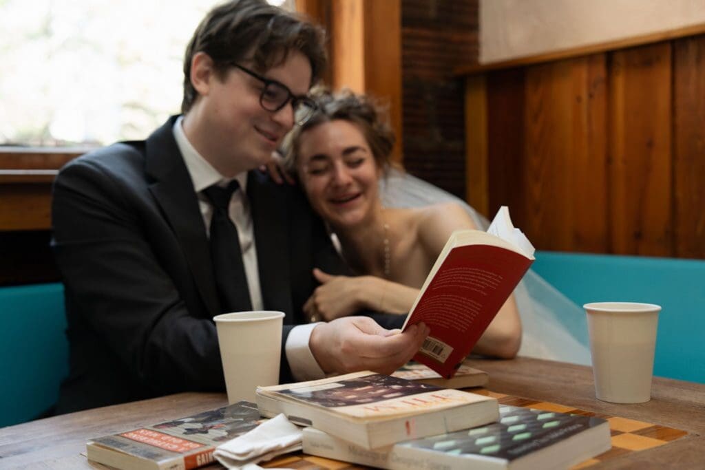 Couple reading a book together dressed up as a Bride and groom inside a cafe