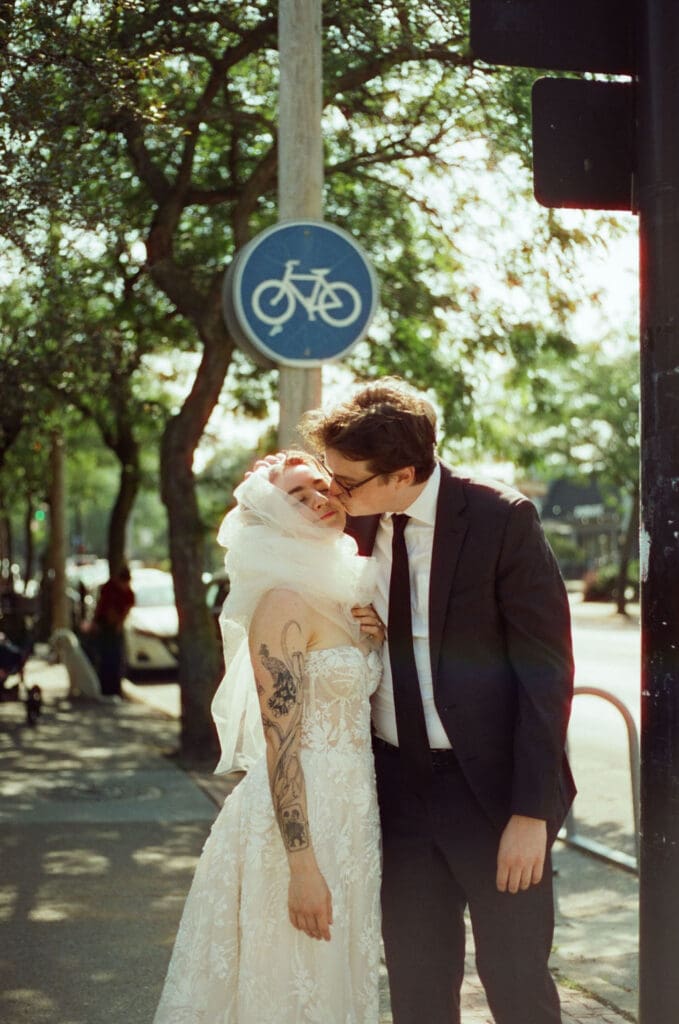 Vintage film photo of a bride and groom outside a cafe, the bride is being goofy and the groom is kissing her on the cheek