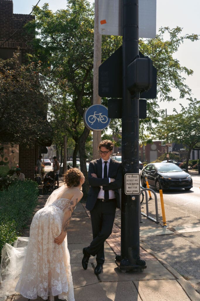 photo of a bride and groom outside a cafe, the bride is being goofy and the groom is leaning on a lamppost smiling at her