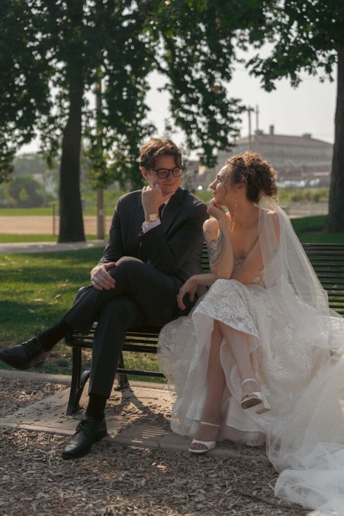 editorial photo of a bride and groom sitting on a playground table outside looking at each other