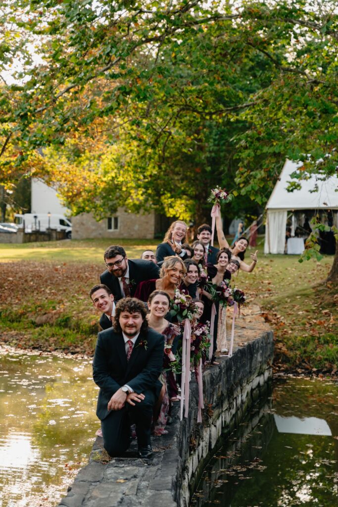 Bridal party posing for a photo on a stone wall above a pond