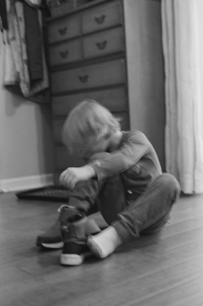 black and white film photo of a boy putting on boots