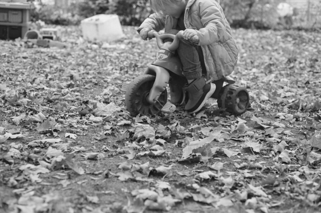 black and white film photo of a boy riding his tricycle